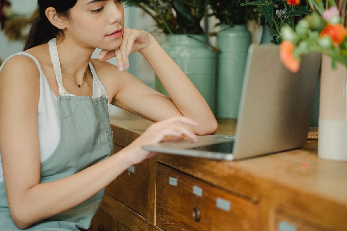 A florist at a laptop on the shop counter, flowers behind her