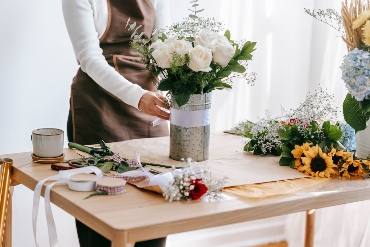 A florist at a wooden bench, finishing an arrangement of white roses